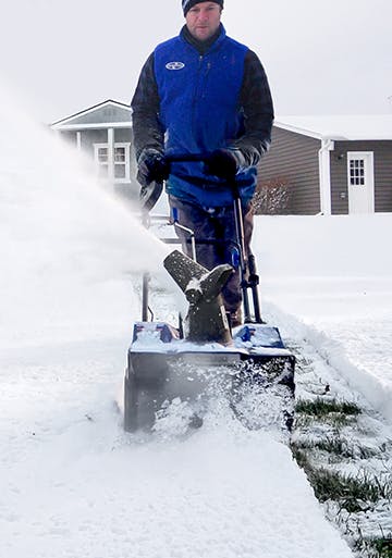 Man using the Snow Joe 48-volt Cordless 18-inch Snow Blower Kit to throw snow and make a pathway.